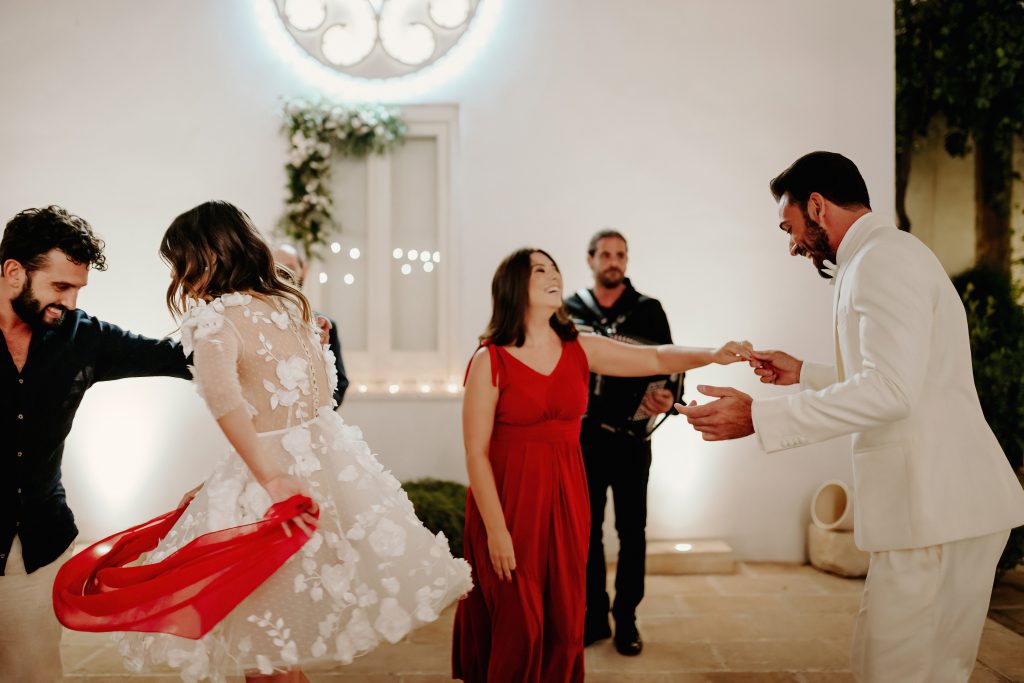 La sposa fa roteare un velo rosso ballando la pizzica con gli invitati, davanti al musicista con la fisarmonica