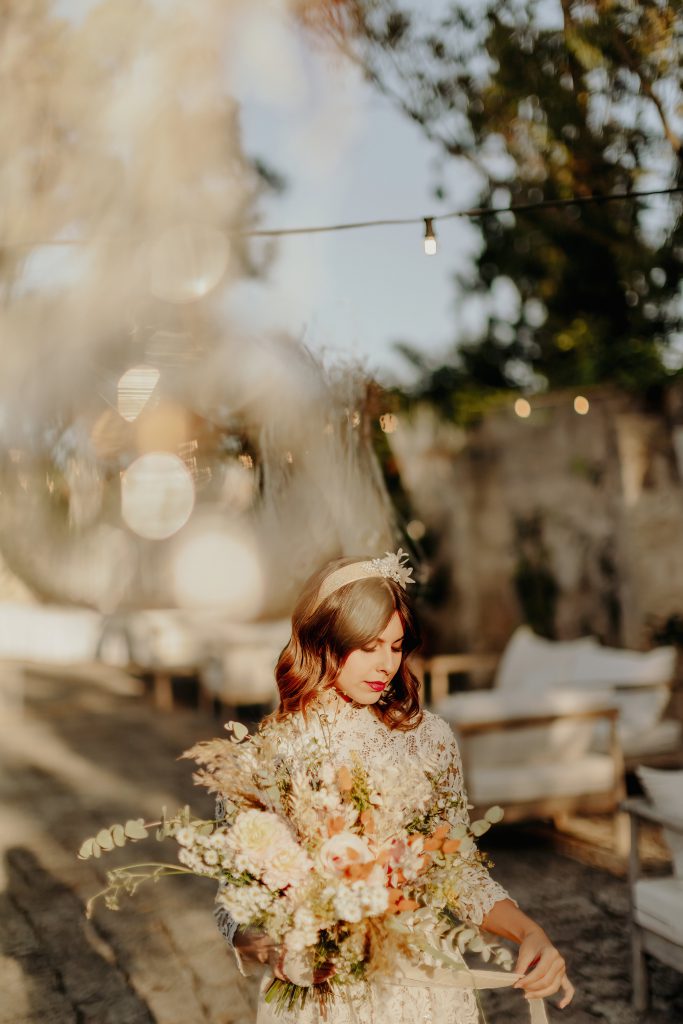 La sposa nella corte al tramonto con un grande bouquet di fiori secchi color pesca